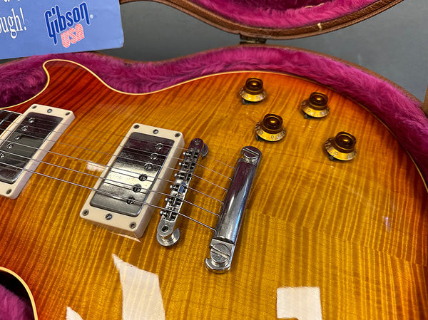 Close-up of sunburst Gibson electric guitar body showing dual humbucker pickups, chrome bridge and tailpiece, and amber control knobs in pink lined guitar case