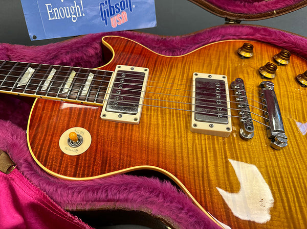 Close-up of sunburst Gibson Les Paul electric guitar with dual humbucker pickups, cream pickup frames, and amber control knobs, resting in a pink plush-lined hard case with Gibson USA card visible.