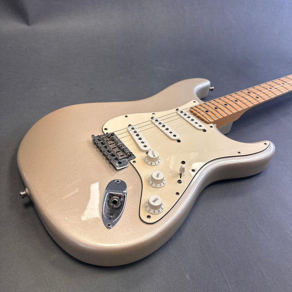 Electric guitar with a pearl white body, three single-coil pickups, white pickguard, and maple neck lying on a gray surface.