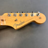 Close-up of Fender Stratocaster guitar headstock in natural wood finish with chrome tuning pegs on grey background