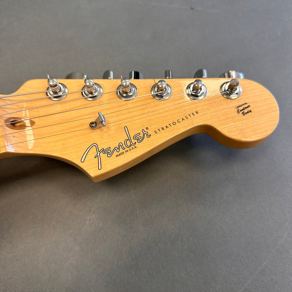 Close-up of Fender Stratocaster guitar headstock in natural wood finish with chrome tuning pegs on grey background