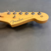 Close-up of natural wood Fender Stratocaster guitar headstock with tuning pegs and strings on gray background