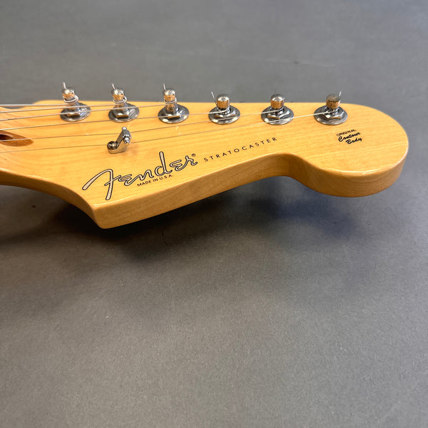 Close-up of natural wood Fender Stratocaster guitar headstock with tuning pegs and strings on gray background