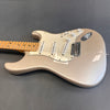 Electric guitar with metallic silver body, white pickguard, three single-coil pickups, maple neck, and tone and volume knobs on a gray background