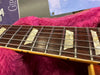 Close-up of guitar fretboard with pearl block inlays and metal strings on a dark wood neck, resting on pink fuzzy fabric.