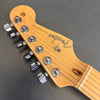 Close-up of Fender Stratocaster guitar headstock with chrome tuning pegs and natural wood finish on gray background