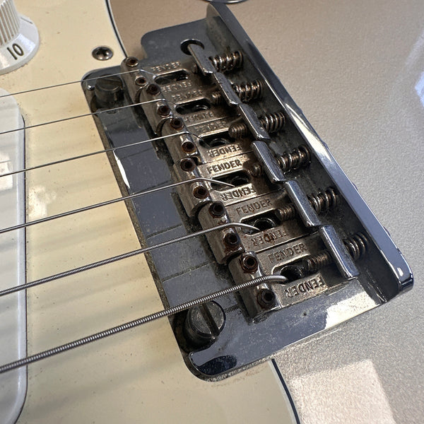 Close-up of Fender guitar bridge with six strings and individual metal saddles on a cream electric guitar body