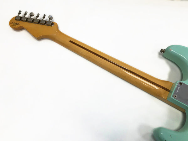 Back view of maple neck and vintage tuners on a light blue Fender Stratocaster electric guitar against a white background