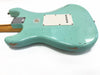 Back of vintage-style seafoam green electric guitar body with white plastic tremolo cavity cover and visible wear and paint chips on a white background