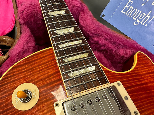 Close-up of electric guitar neck and body showing pearl inlays, pickup, and selector switch on a sunburst finish guitar inside a plush pink case