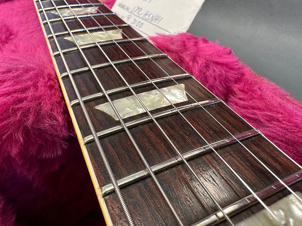 Close-up of rosewood guitar fretboard with mother-of-pearl block inlays and metal frets on electric guitar neck, resting on pink plush guitar case lining