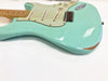 Close-up view of seafoam green electric guitar body with vintage white pickguard, three single-coil pickups, maple fretboard, and visible wear and paint chipping near the edges on white background