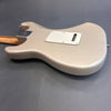 Back view of a cream-colored electric guitar body with a white plastic backplate and light wooden neck on a gray surface