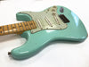 Seafoam green electric guitar with maple fretboard and three single-coil pickups, vintage wear and dents visible on guitar body.