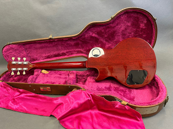 Electric guitar back view showing mahogany body and neck inside open brown hard case with bright pink plush interior lining and matching pink cover cloth.