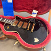 Black Gibson electric guitar with gold hardware and three pickups in a pink plush-lined hard case with Gibson USA tag and blue certificate