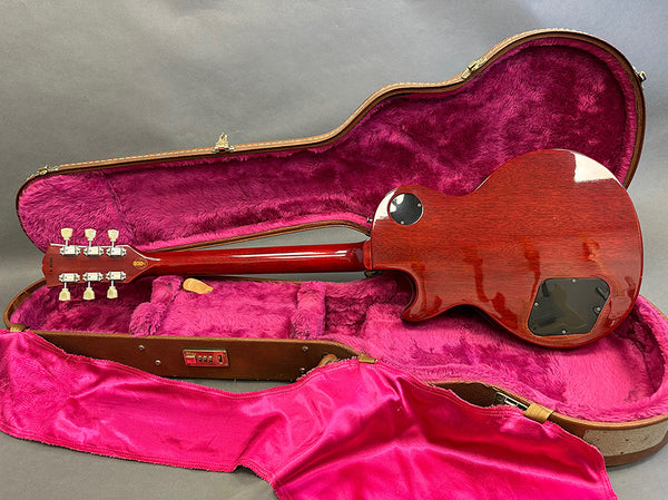 Back view of cherry red electric guitar inside open hard case with plush pink interior lining and matching pink cover, showcasing mahogany body and chrome tuning pegs
