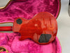 Back of red electric guitar with black control cavity covers, lying in pink plush guitar case interior