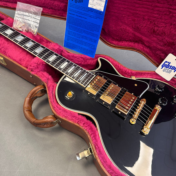 Gibson electric guitar with black finish, three gold humbucker pickups, toggle switch, and black control knobs inside a brown hard case lined with pink plush interior