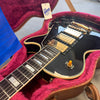 Close-up of black Gibson electric guitar with gold hardware and three humbucker pickups in pink plush-lined brown hard case with Gibson USA tag and blue warranty card