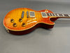 Electric guitar with flame maple top and amber sunburst finish, featuring humbucker pickups and four amber control knobs on gray background