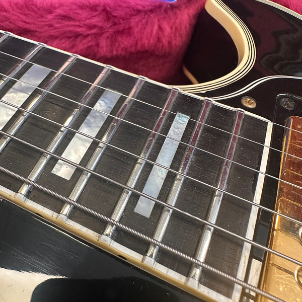 Close-up of black electric guitar fretboard with mother of pearl inlays and metal strings on a red fabric background