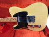 Yellow vintage-style electric guitar with black pickguard and maple neck resting in red velvet-lined case