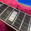 Close-up of guitar fretboard showing mother of pearl rectangular inlays and steel strings on dark wood fingerboard, resting inside pink plush-lined guitar case.