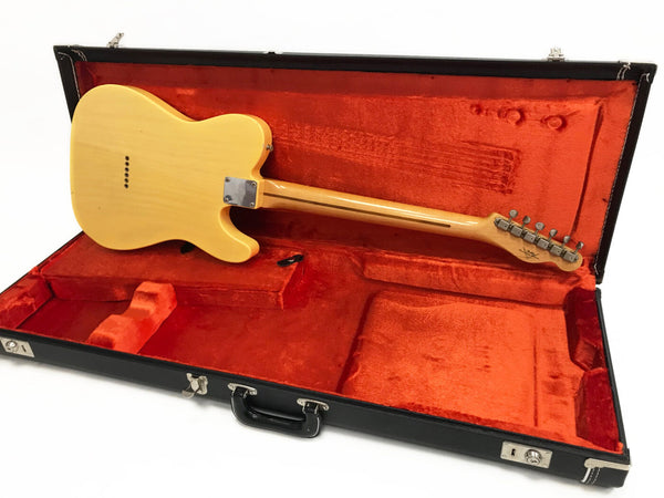 Vintage electric guitar with blonde finish lying in open black hard case with orange plush interior, back view showing neck and tuning pegs