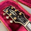 Close-up of Gibson Les Paul Custom guitar headstock with vintage tuners in a plush red guitar case interior
