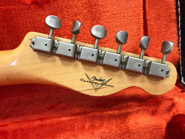 Close-up of Fender Custom Shop guitar headstock with vintage-style tuning pegs on orange plush case lining