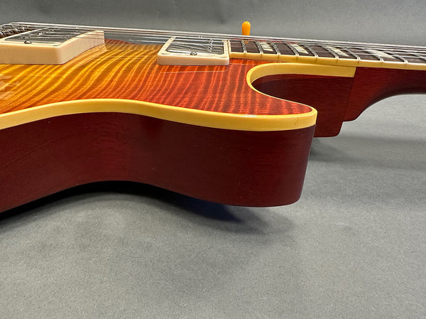 Close-up of sunburst electric guitar body with cream binding and pearl inlay block fretboard on gray background