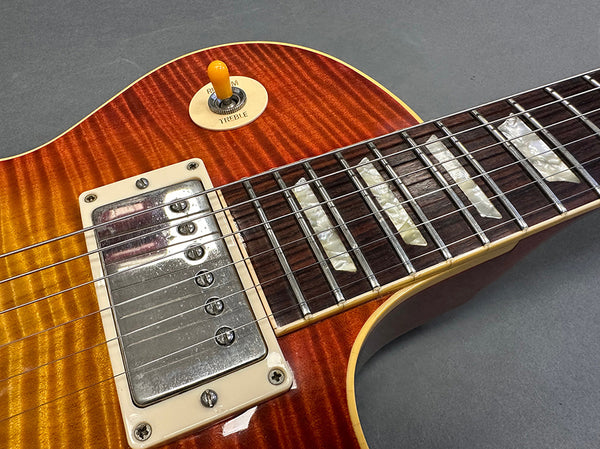 Close-up of sunburst electric guitar body showing chrome humbucker pickup, pearl inlay fretboard, and treble toggle switch on a flamed maple top