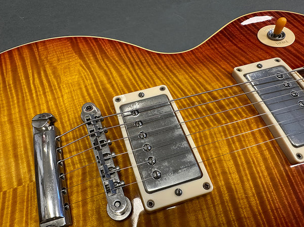 Close-up of amber sunburst electric guitar body showing metal bridge, chrome humbucker pickups, and strings on flamed maple top.