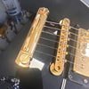 Close-up of black electric guitar bridge and tailpiece with gold hardware and six strings, showing volume knob and pickup details
