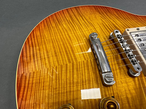 Close-up of a sunburst electric guitar body showing the flamed maple top, chrome bridge, pickup, and amber control knobs on a gray background.