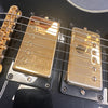 Close-up of gold humbucker pickups and bridge on black electric guitar with six strings at Coffee House Guitars.
