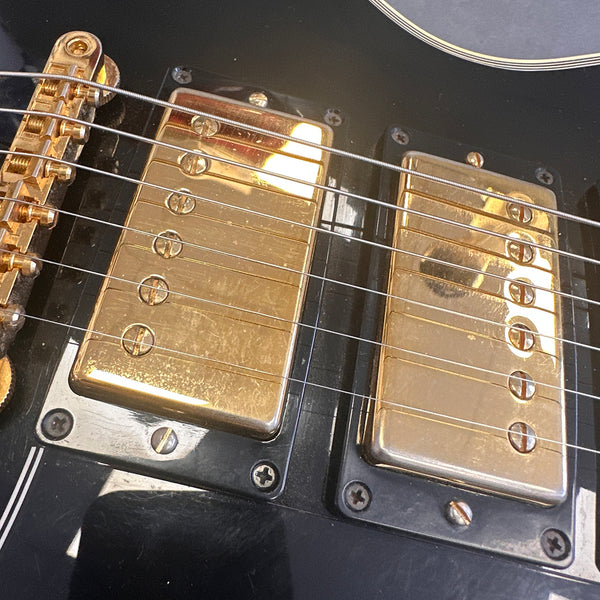 Close-up of gold humbucker pickups and bridge on black electric guitar with six strings at Coffee House Guitars.