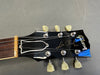 Close-up of Gibson Les Paul model guitar headstock with tuning pegs and strings on gray surface
