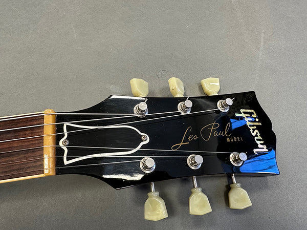 Close-up of Gibson Les Paul model guitar headstock with tuning pegs and strings on gray surface