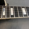 Close-up of electric guitar fretboard with rectangular pearl inlays and metal frets, showcasing strings and cream binding.