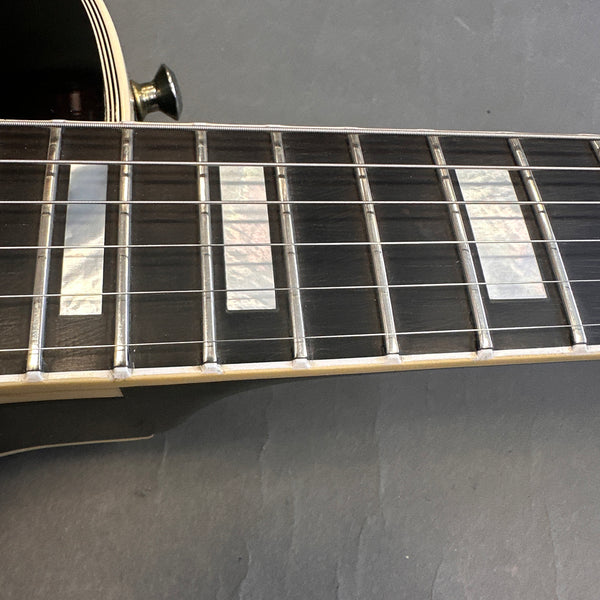 Close-up of electric guitar fretboard with rectangular pearl inlays and metal frets, showcasing strings and cream binding.