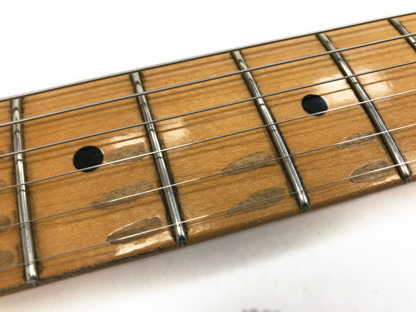 Close-up of maple guitar fretboard with dot inlays and frets, showing guitar strings and wood grain texture