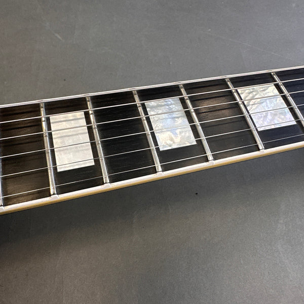 Close-up of guitar neck showing rectangular mother-of-pearl inlays and steel strings on dark wood fretboard