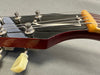 Close-up of vintage guitar headstock with tuning pegs, steel strings, and black finish, showing wear and string winding detail