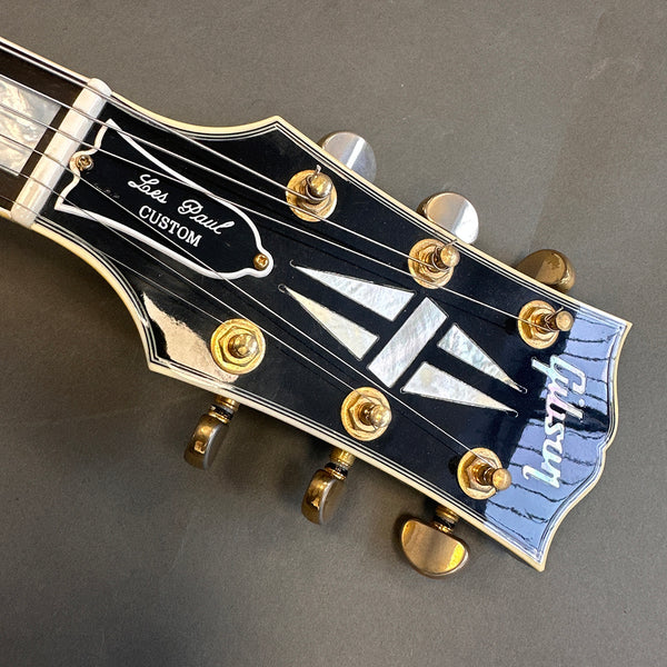 Close-up of Gibson Les Paul Custom guitar headstock with mother-of-pearl inlay and gold tuning pegs on a black background
