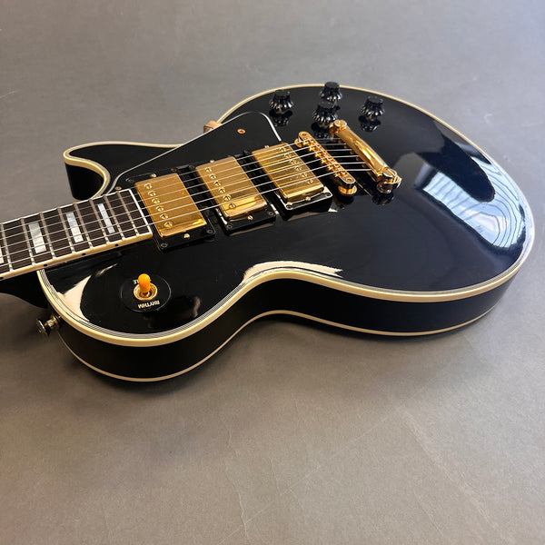 Black electric guitar with gold pickups and bridge on grey background, Les Paul style guitar with cream binding and black control knobs