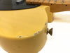 Close-up of yellow electric guitar body corner with visible wear and paint chipping near strap button, maple neck and fretboard visible in background.