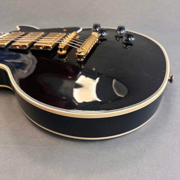 Close-up of black electric guitar body with gold hardware and cream binding on a gray background