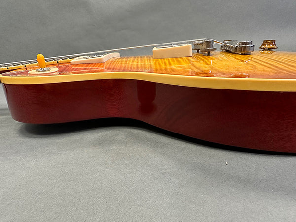 Close-up side view of electric guitar body with sunburst finish and cream binding on grey background